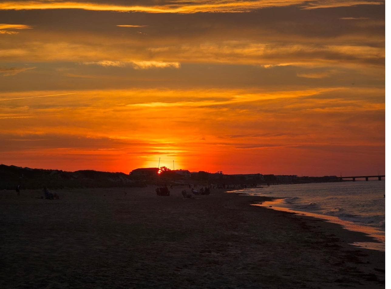 Families and friends scattered along the beach as the sun sets over Shore Drive