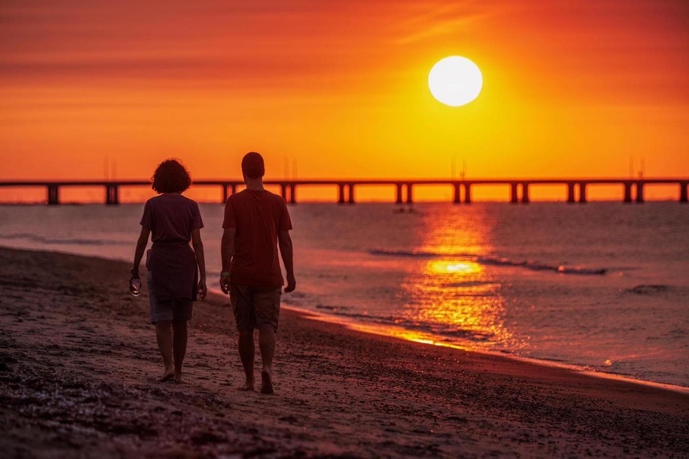 Two people walking the beach at sunset with the Lesner Bridge in the distance